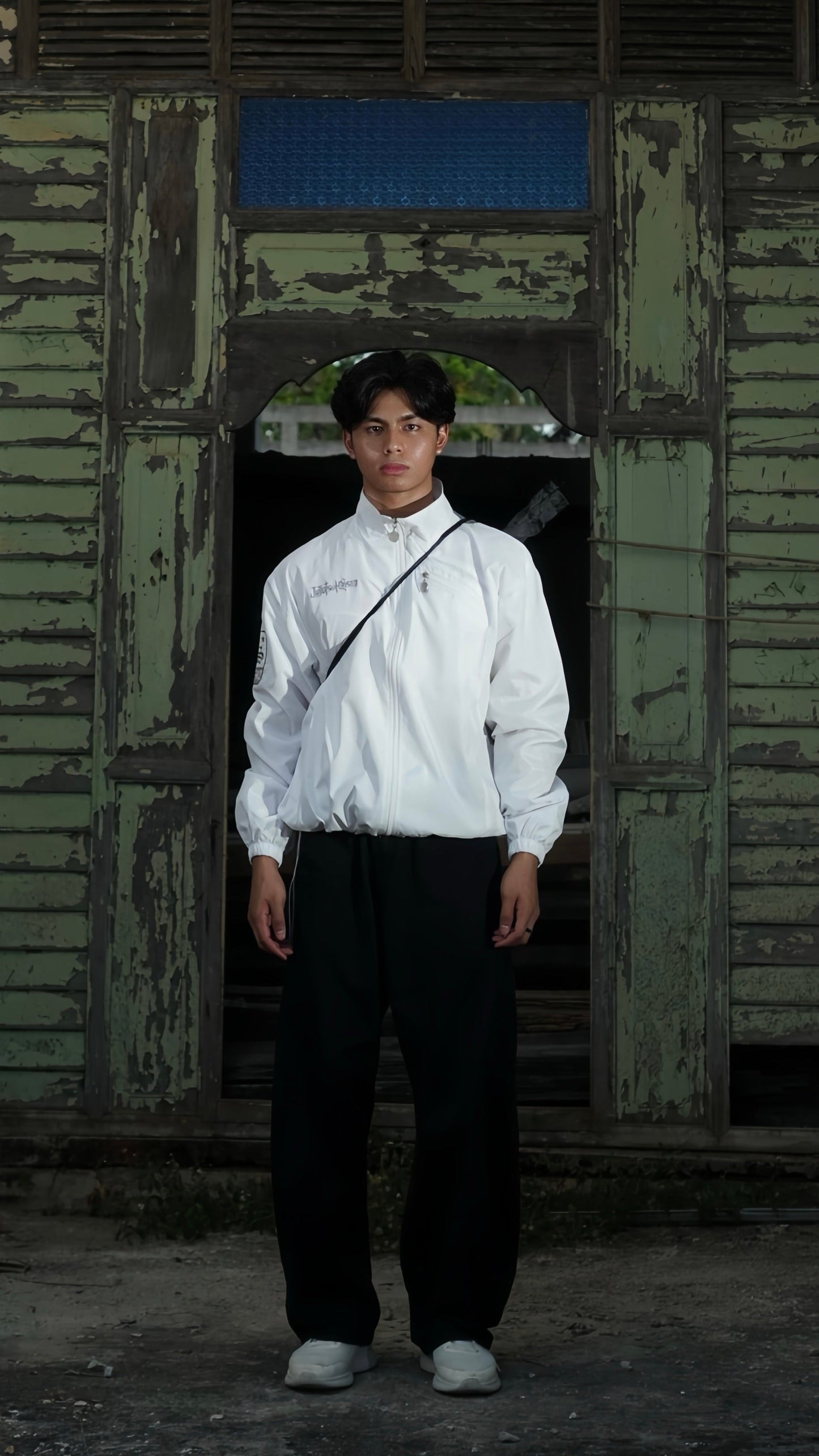 Person wearing a white shirt and dark pants standing in front of a weathered wooden door.